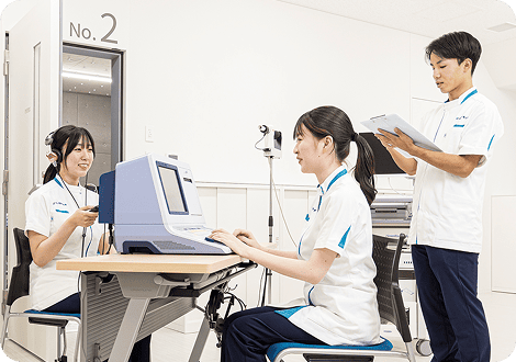 装置を用いて言語聴覚の練習をする女子学生2人と記録する男子学生