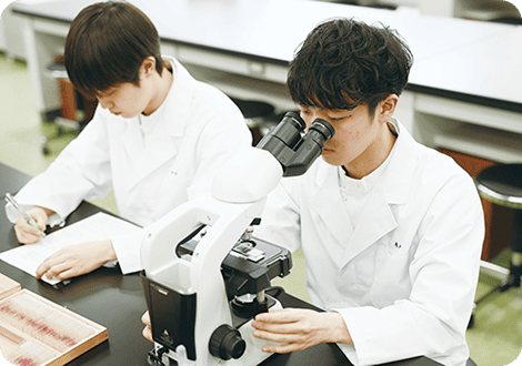 顕微鏡で検査を行う男子学生と記録を行う男子学生
