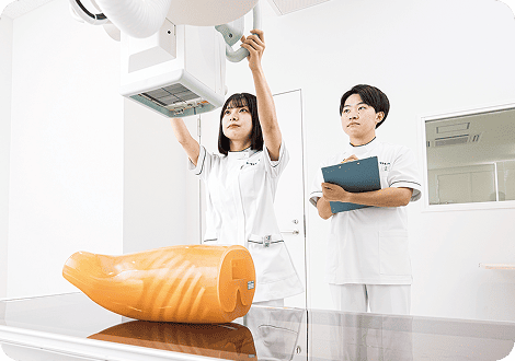 人体モデルを用いてレントゲンの実習を行う男子学生と女子学生
