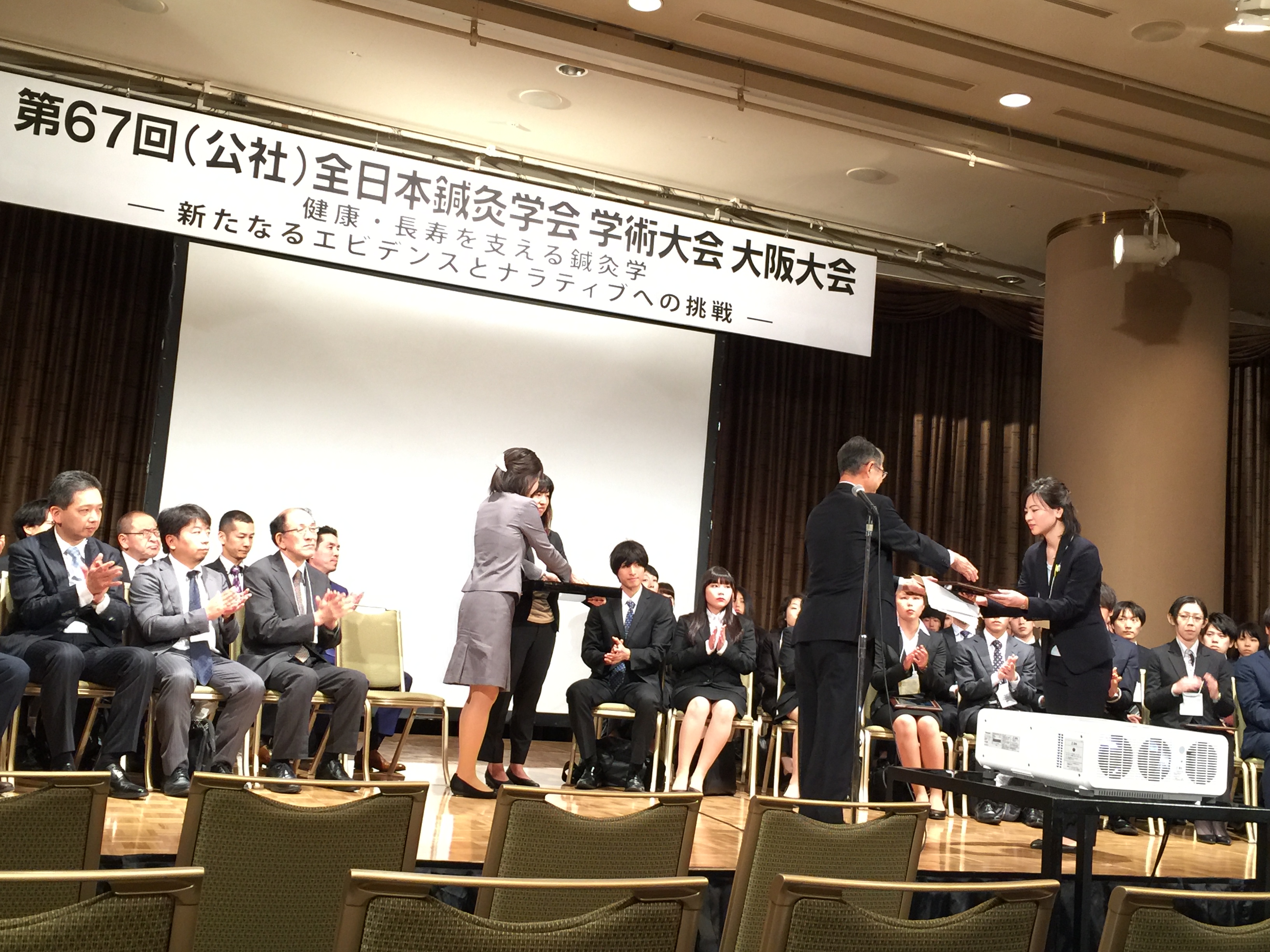 大阪大会会頭の荻原俊男学長から優秀賞の盾を受け取る西村志帆さん