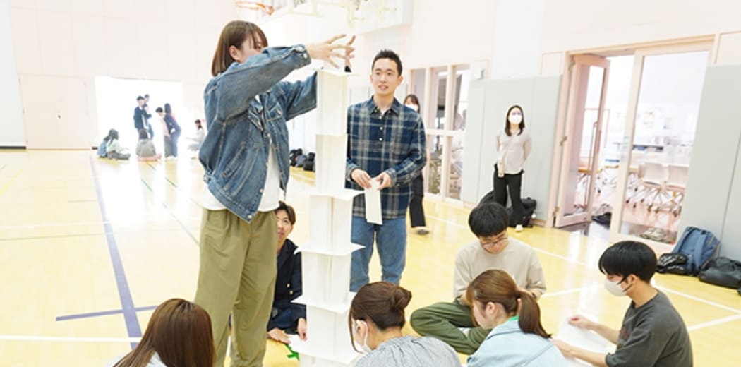 男女学生が協力して高い塔を組み立てる課題に取り組んでいます。