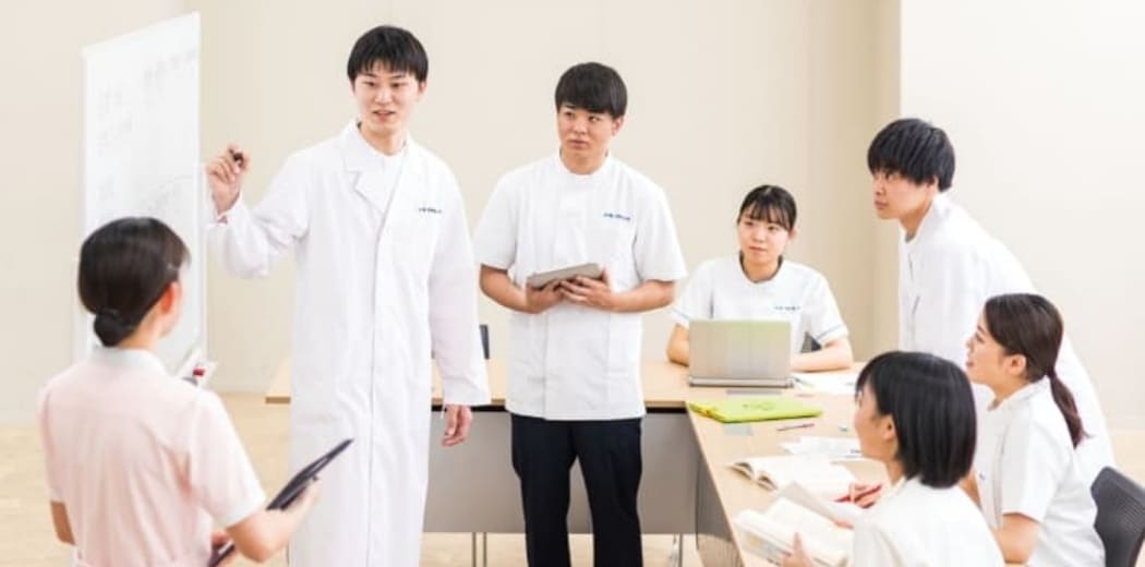 男女学生が会議室で壁に貼り出した説明図を囲んで議論しています。